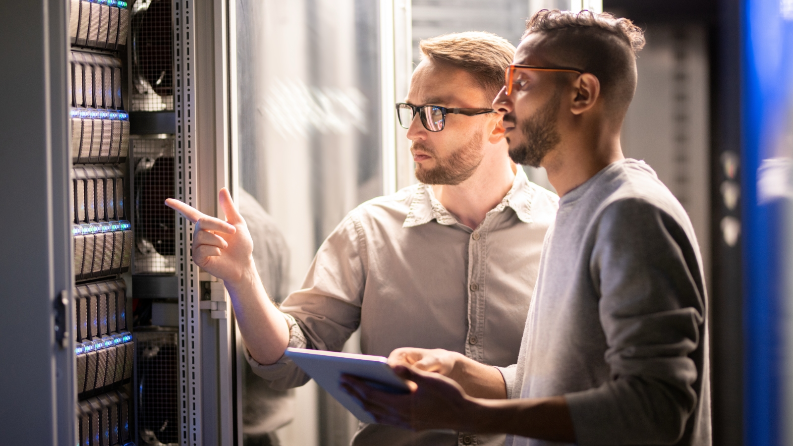 Two men examine storage devices mounted on a rack.
