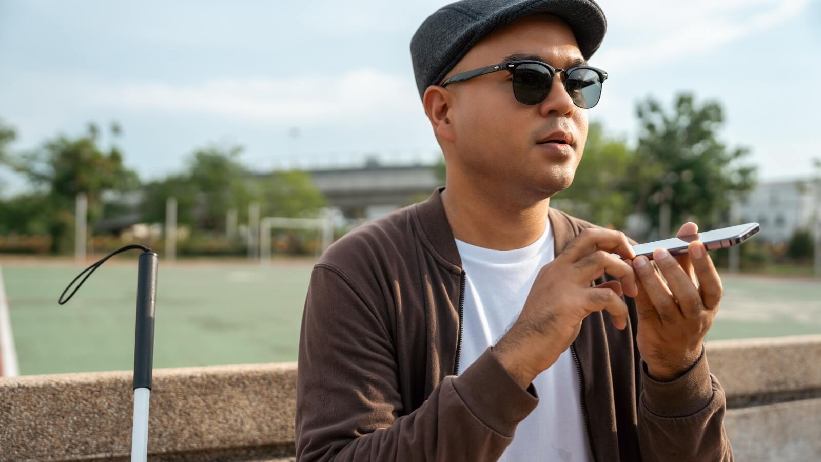 A blind man is sitting outside on a park bench and uses the screen readeron his smartphone.