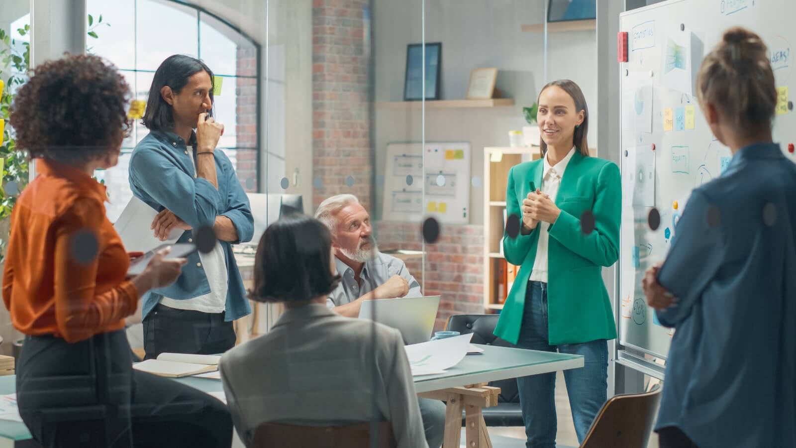 A woman presents a Gantt chart on a large screen in a meeting with three other people.